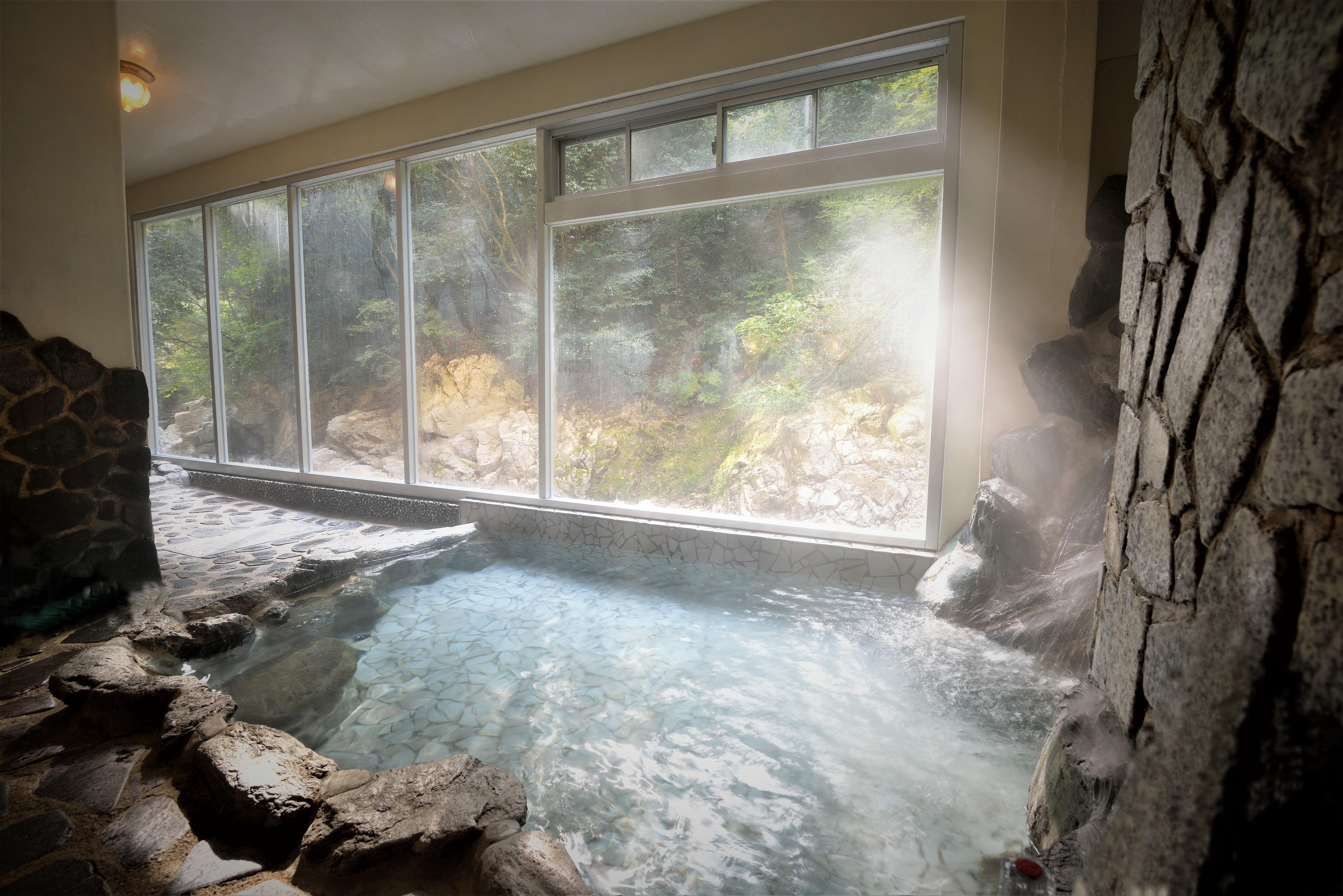 ガラス越しに渓流や草木の彩りを望む温泉